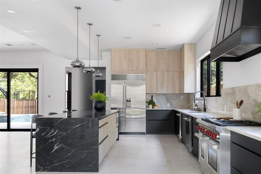 Kitchen with premium appliances, dark stone countertops, custom exhaust hood, and plenty of natural light