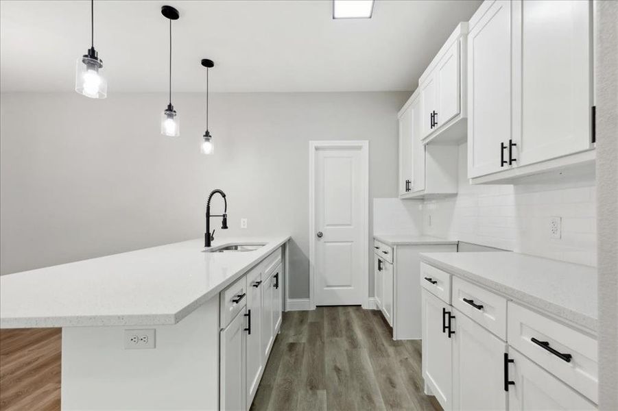 Kitchen with light hardwood / wood-style flooring, sink, backsplash, decorative light fixtures, and white cabinetry