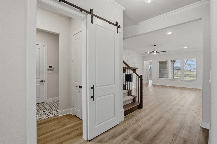 Hall with light wood finished floors, crown molding, a barn door, and recessed lighting