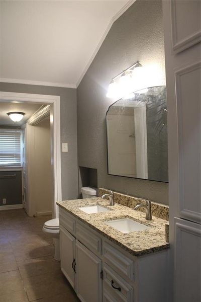 Full bathroom with a textured wall, double vanity, crown molding, and dark tile patterned floors Full bathroom with a textured wall, double vanity, crown molding, and dark tile patterned floors