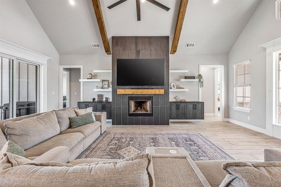 Living area with high vaulted ceiling, light wood-style flooring, a fireplace, a ceiling fan, and beamed ceiling