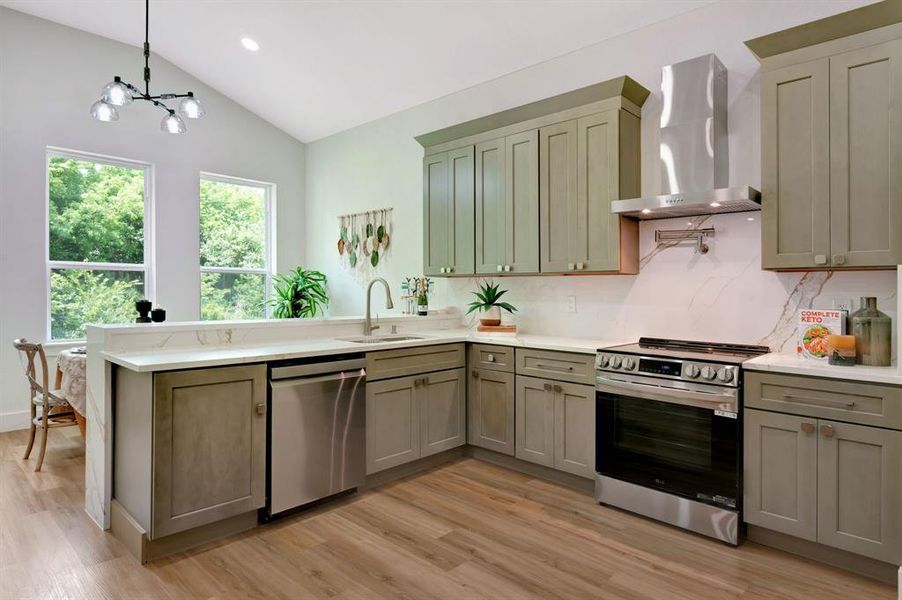 Kitchen featuring vaulted ceilings, light green cabinetry, stainless steel appliances, a white countertop, and wood-finish flooring Kitchen featuring vaulted ceilings, light green cabinetry, stainless steel appliances, a white countertop, and wood-finish flooring