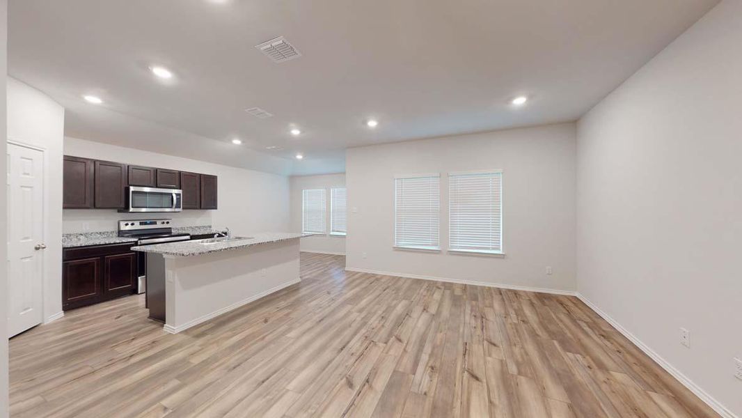 Open-concept living space featuring wood-finish flooring, recessed lighting, and multiple windows with blinds