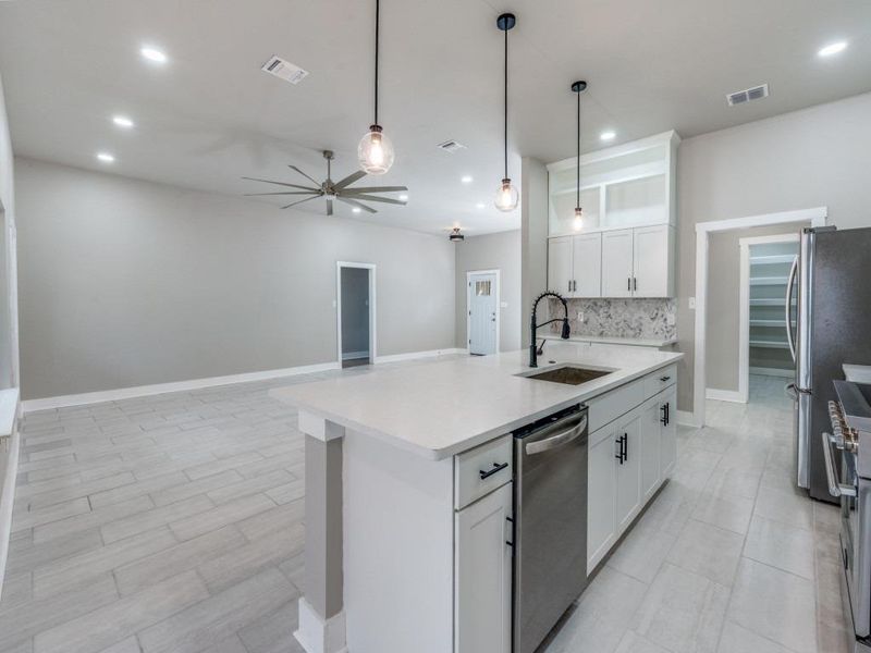 Kitchen with ceiling fan, stainless steel appliances, white cabinetry, pendant lighting, and open floor plan