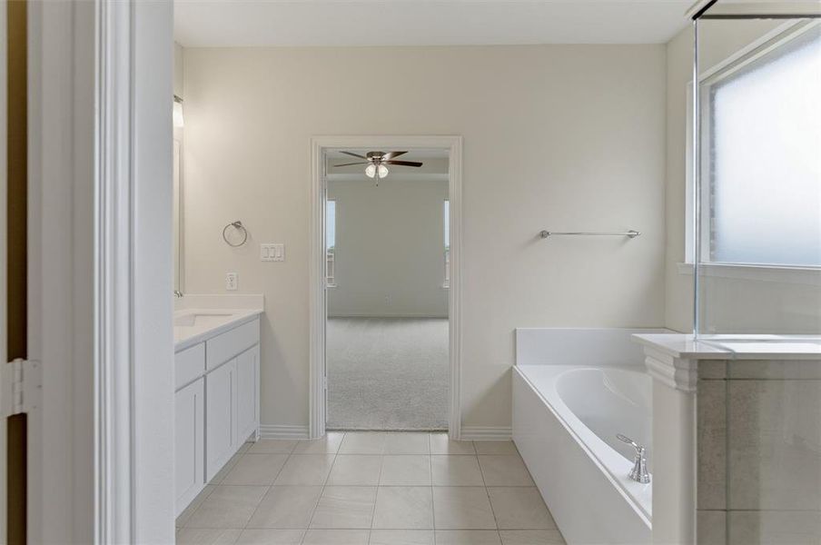Bathroom featuring a white dual vanity with undermount sinks, a built-in soaking tub, a tiled shower with glass enclosure, and light tile flooring