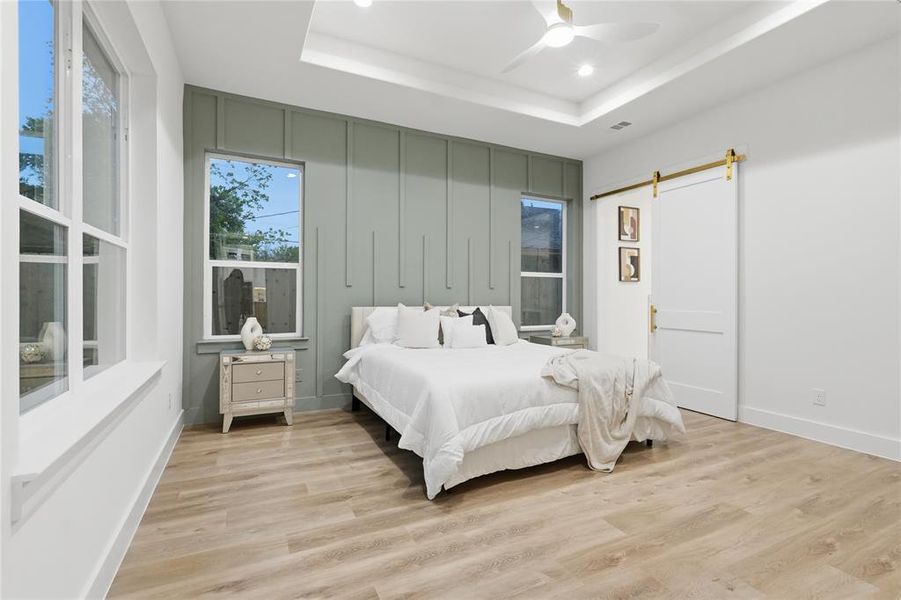 Bedroom featuring a barn door, light wood-style floors, a raised ceiling, a ceiling fan, and recessed lighting