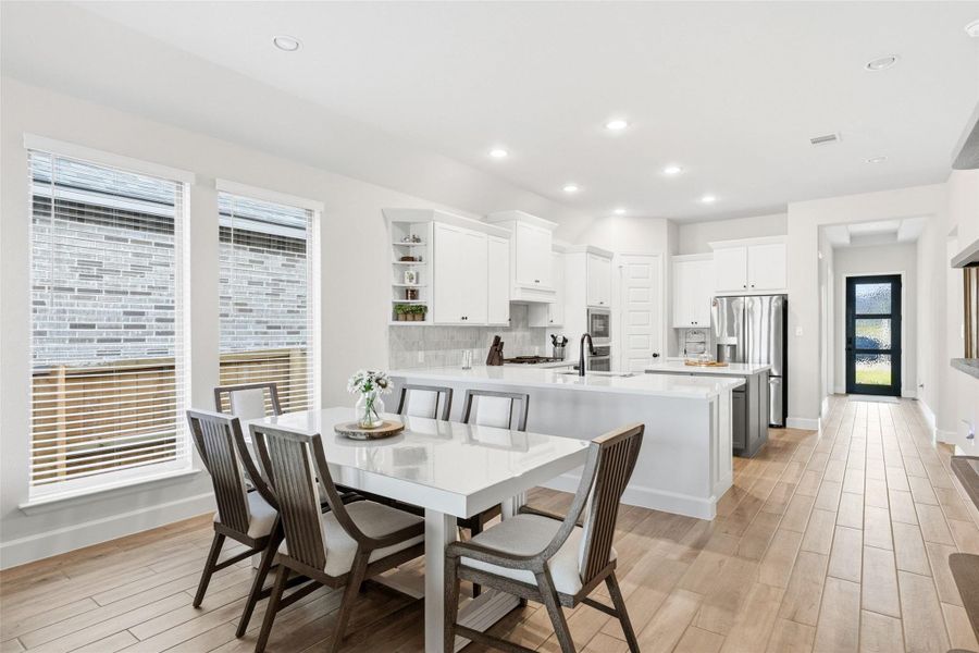 Open-concept kitchen and dining area featuring light-toned wood-finish flooring, recessed lighting, white cabinetry, and stainless steel appliances
