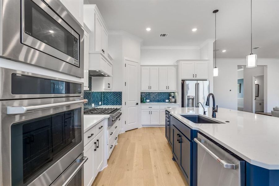 Kitchen with appliances with stainless steel finishes, backsplash, sink, decorative light fixtures, and white cabinetry