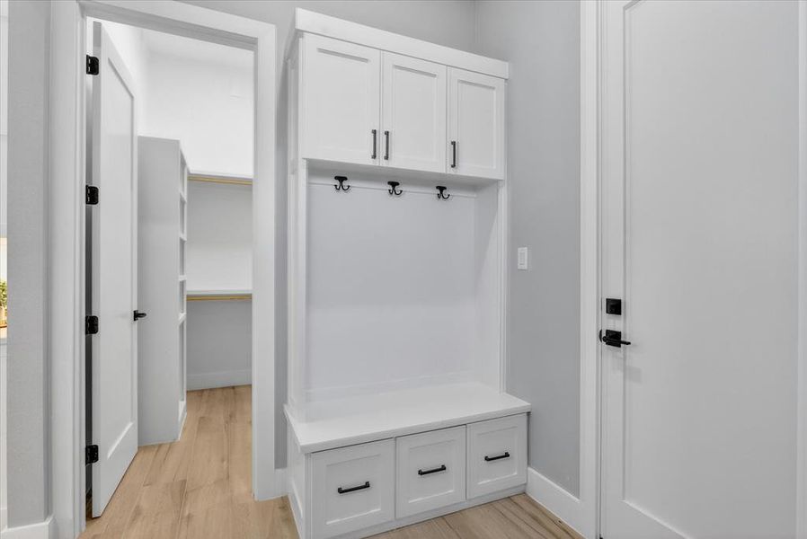 Built-in mudroom cabinetry featuring upper storage, coat hooks, and bench seating with drawers