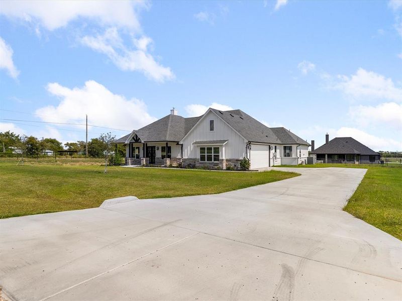 View of front of house with stone siding, a front lawn, concrete driveway, board and batten siding, and covered porch View of front of house with stone siding, a front lawn, concrete driveway, board and batten siding, and covered porch