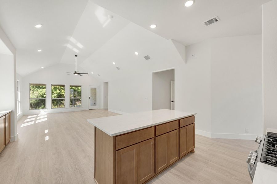 Open kitchen and living area with wood island, vaulted ceiling, ceiling fan, and light hardwood floors