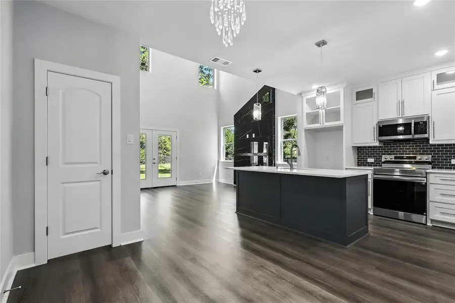 Kitchen with stainless steel appliances, white cabinets, glass insert cabinets, decorative backsplash, and dark wood finished floors