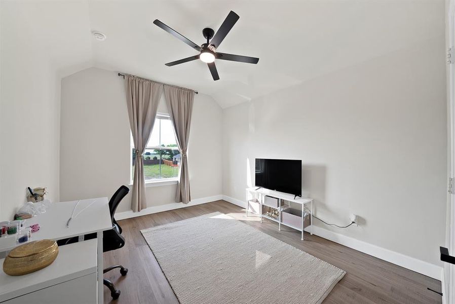 Vaulted ceiling with a contemporary ceiling fan, wood-finish flooring, and a large window with neutral drapery Vaulted ceiling with a contemporary ceiling fan, wood-finish flooring, and a large window with neutral drapery
