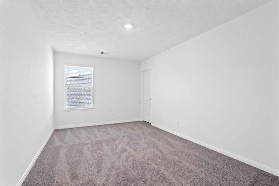 This secondary bedroom offers comfort and style with plush carpeting, neutral paint tones, recessed lighting, a large window with blinds, and a walk-in closet.