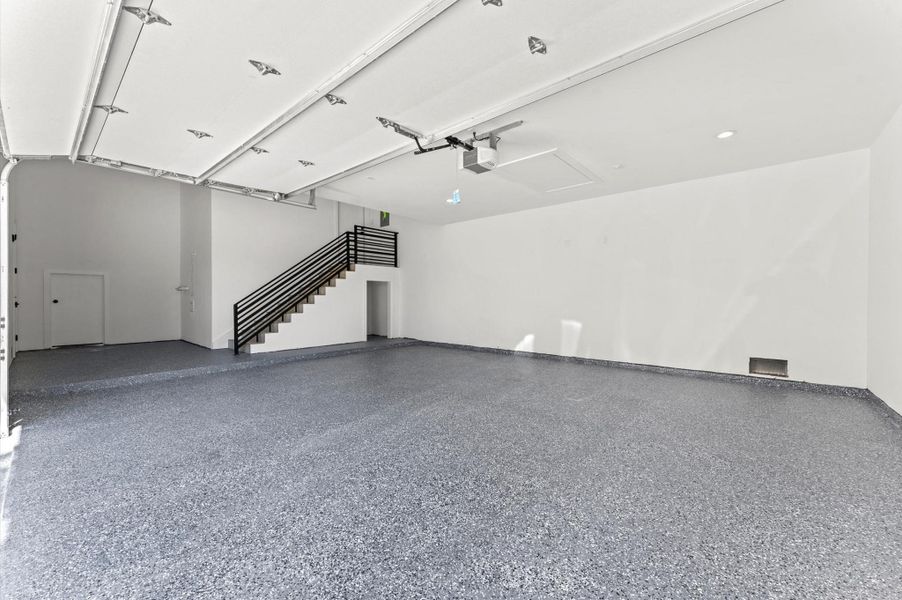 Spacious, modern garage with a clean epoxy floor and ample lighting. It features a staircase leading to the first level, offering additional storage.