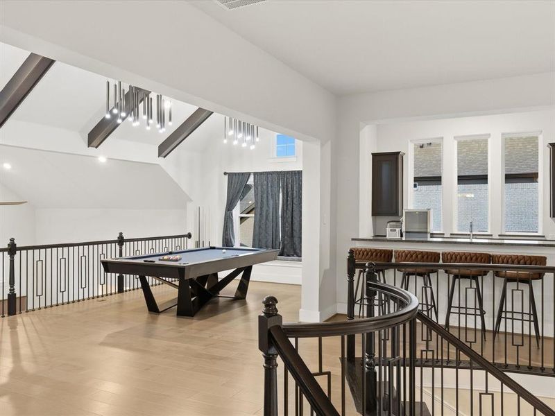 Loft space featuring light wood-finish flooring, a contemporary billiards table, and a wet bar with dark cabinetry and countertop Loft space featuring light wood-finish flooring, a contemporary billiards table, and a wet bar with dark cabinetry and countertop