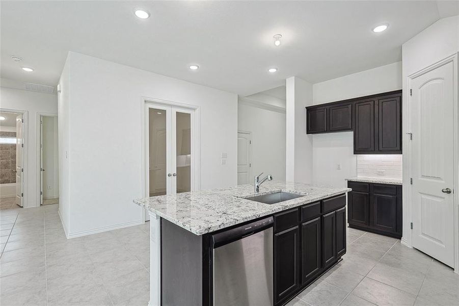 Kitchen featuring light stone counters, light tile patterned floors, sink, a kitchen island with sink, and dishwasher