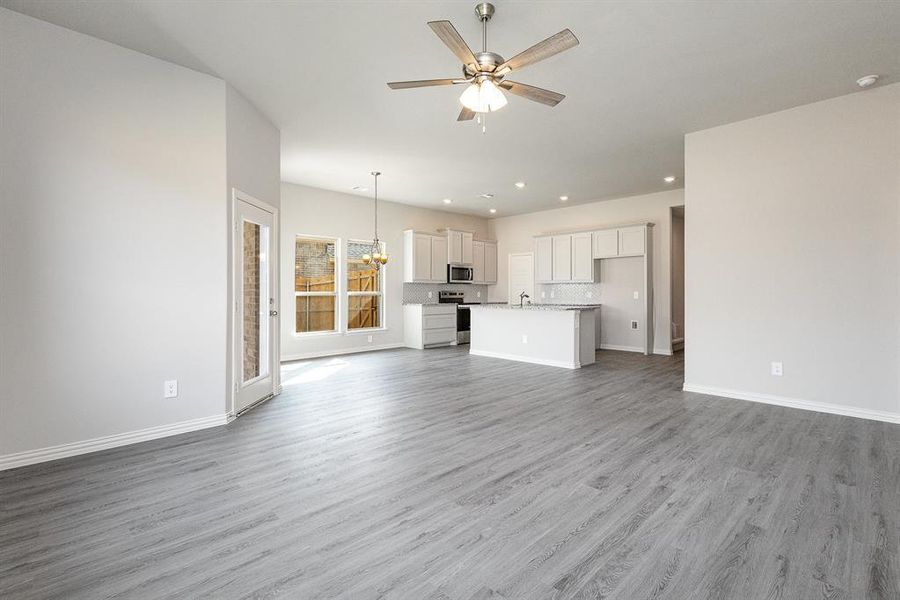 Unfurnished living room featuring ceiling fan with notable chandelier and wood-type flooring