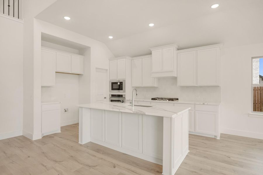 White kitchen with large center island, marble countertops, white cabinets, and stainless steel appliances on light wood floors
