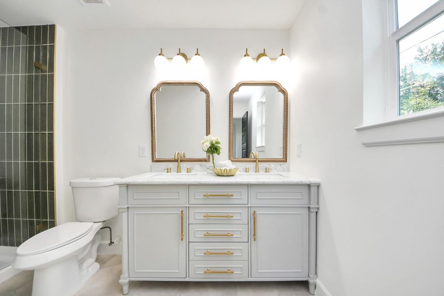 This thoughtfully designed bathroom blends classic elegance with modern flair. Dual arched mirrors, brass fixtures, and soft pendant lighting create a polished, timeless look. The custom vanity offers generous storage, while natural light from the oversized window brings a bright, refreshing feel to the space.