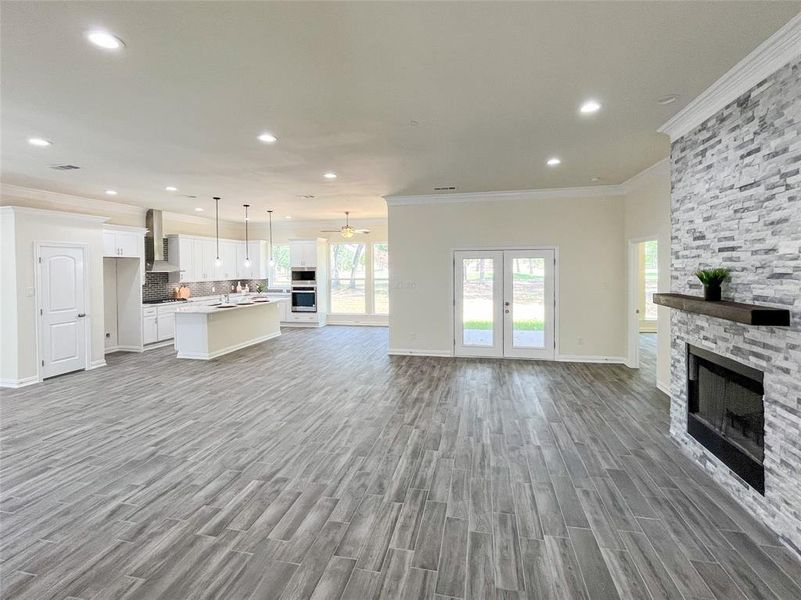 Unfurnished living room featuring a stone fireplace, light hardwood / wood-style flooring, crown molding, and french doors