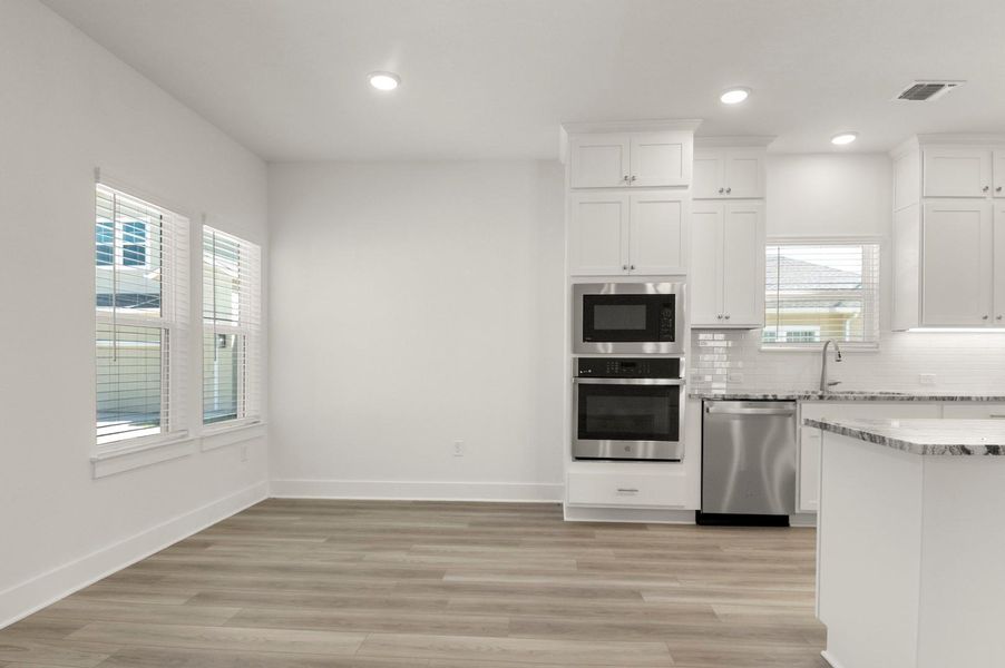 Kitchen with white cabinetry, stainless steel appliances, decorative backsplash, light stone countertops, and light wood finished floors Kitchen with white cabinetry, stainless steel appliances, decorative backsplash, light stone countertops, and light wood finished floors