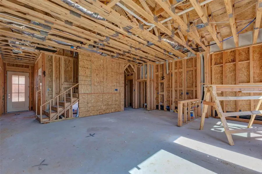 Main-level interior framing view highlighting the staircase, future living area, kitchen placement, and open layout. Exposed beams, electrical rough-ins, and structural framing give buyers a clear look at the home’s construction quality and flow, while the large open space helps showcase the potential for everyday living and entertaining. Main-level interior framing view highlighting the staircase, future living area, kitchen placement, and open layout. Exposed beams, electrical rough-ins, and structural framing give buyers a clear look at the home’s construction quality and flow, while the large open space helps showcase the potential for everyday living and entertaining.
