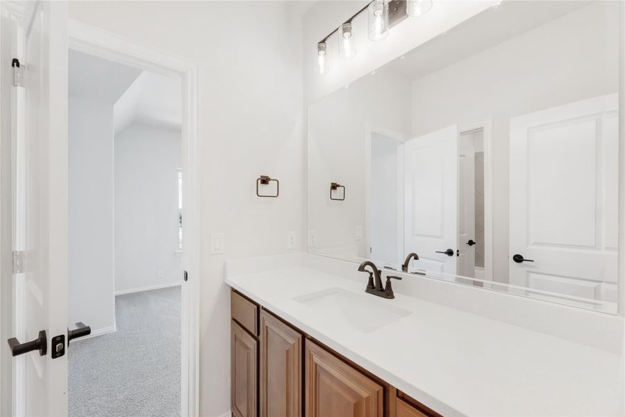 Bathroom vanity with white countertop, wood cabinets, large mirror, and bronze fixtures Bathroom vanity with white countertop, wood cabinets, large mirror, and bronze fixtures