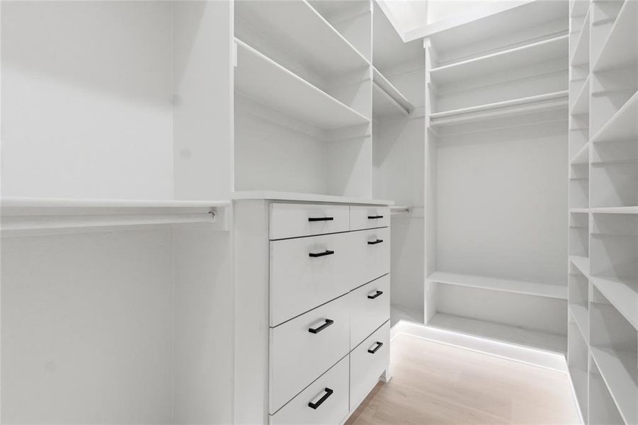 Custom white cabinetry featuring multiple shelving units, hanging rods, an integrated dresser with six drawers, and matte black hardware Custom white cabinetry featuring multiple shelving units, hanging rods, an integrated dresser with six drawers, and matte black hardware