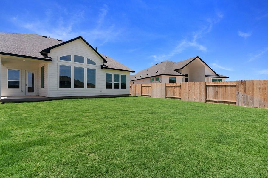 A pristine backyard with lush green grass, perfect for outdoor activities, backs up to a newly constructed home.