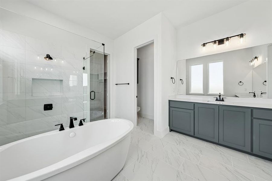 Bathroom with double vanity, a shower stall, a freestanding tub, and light marble finish floors