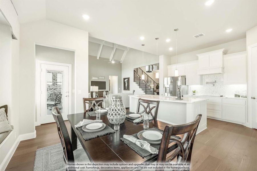 Open-concept dining area with dark wood table and chairs, flowing into white kitchen with island and hardwood floors