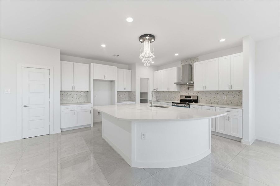 Spacious gourmet kitchen with an oversized curved island and quartz countertops.Crisp white cabinetry, stainless appliances, and designer tile backsplash add elegance.Recessed lighting and a statement chandelier create a bright, modern atmosphere