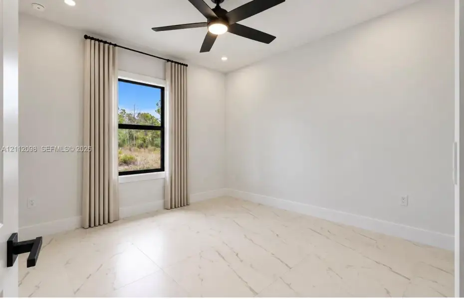 Neutral-toned room featuring large-format tile flooring, a matte black ceiling fan with integrated lighting, and a single-hung window with a black frame Neutral-toned room featuring large-format tile flooring, a matte black ceiling fan with integrated lighting, and a single-hung window with a black frame