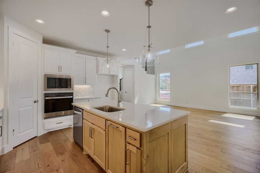 Open-concept kitchen featuring an island with a built-in sink, stainless steel appliances, white shaker cabinetry, and wood-finish flooring