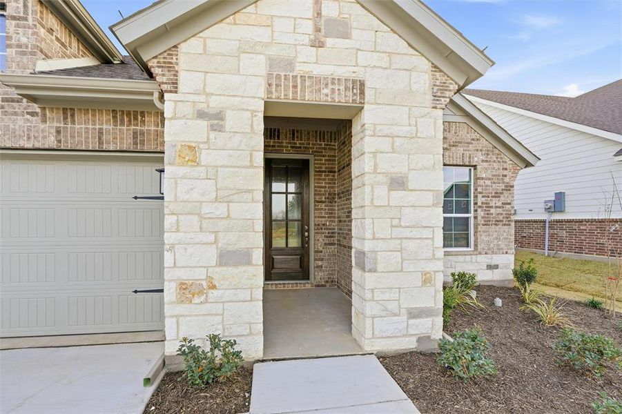 Entrance to property featuring stone siding, a garage, and brick siding