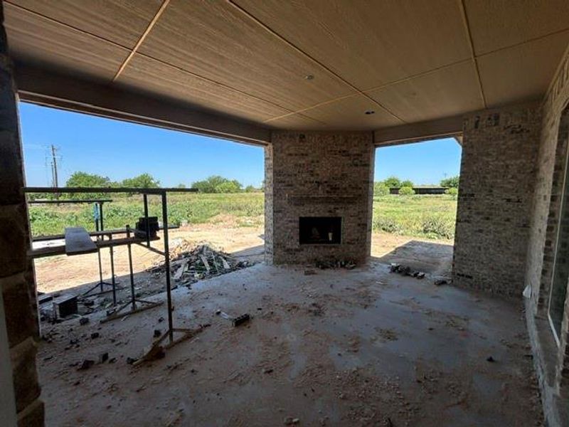 Covered patio featuring a built-in fireplace with a brick surround, exposed brick pillars, a concrete slab floor, and a textured ceiling