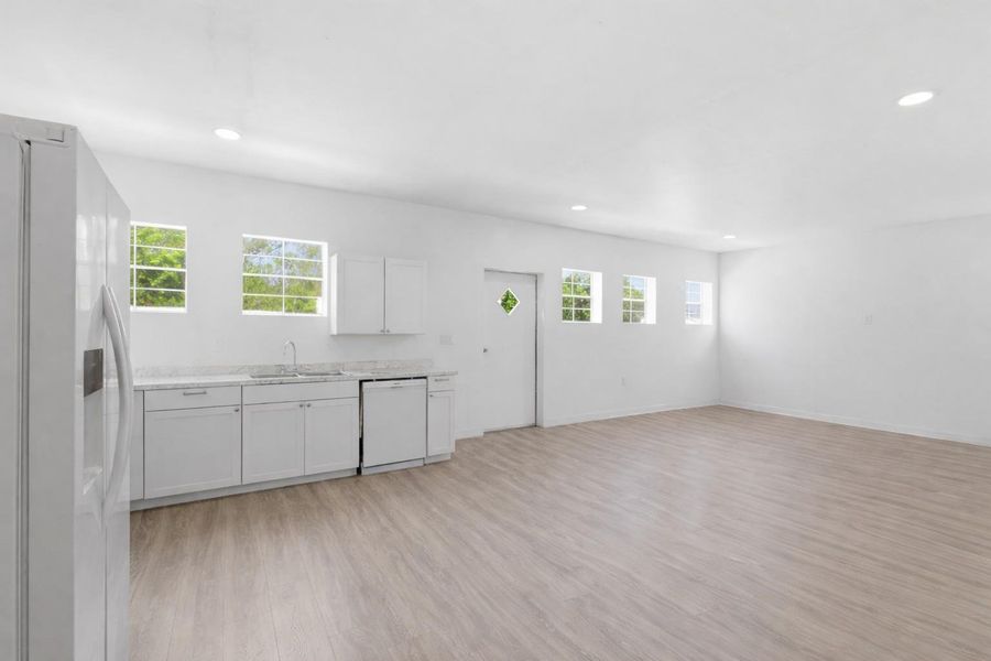 The open concept living area features light-colored flooring, recessed lighting, and a kitchen with white cabinetry, a dishwasher, and a refrigerator