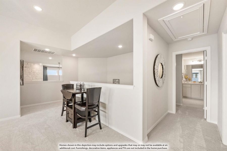 Upstairs loft area with small dining table, carpet flooring, and hallway leading to bathroom