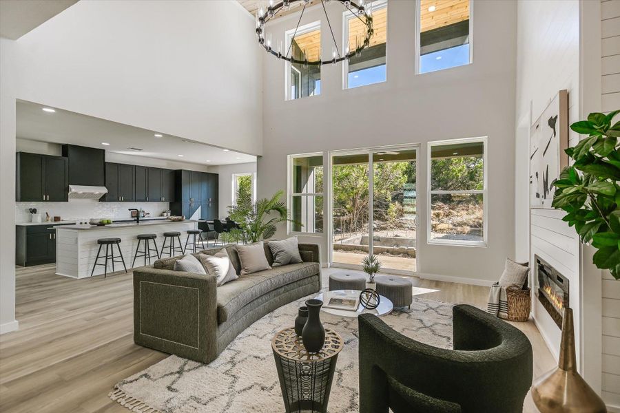 Living area featuring light wood-style floors, a chandelier, a glass covered fireplace, and a towering ceiling