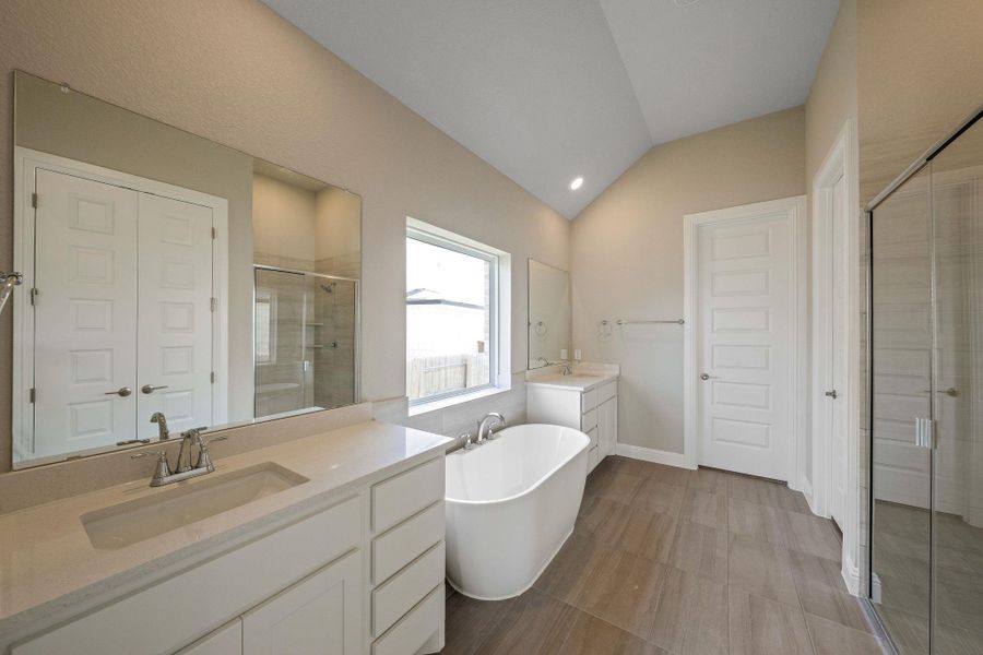 Full bath with vaulted ceiling, a stall shower, two vanities, and a soaking tub
