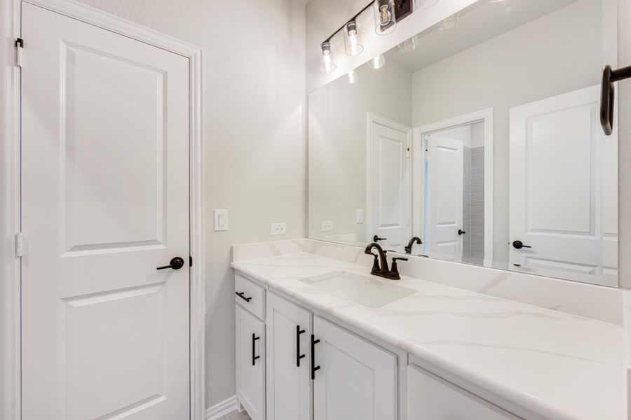 Bathroom with white double vanity, quartz countertop, dark hardware, and large mirror with industrial lighting above Bathroom with white double vanity, quartz countertop, dark hardware, and large mirror with industrial lighting above