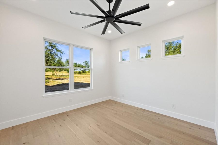 Sun-filled room with hard wood flooring features a modern ceiling fan and multiple windows for abundant natural light. Sun-filled room with hard wood flooring features a modern ceiling fan and multiple windows for abundant natural light.