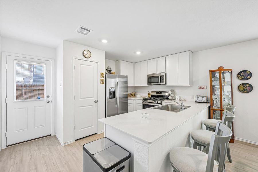 Modern kitchen featuring an island with a stainless steel sink, white cabinetry, a white tile backsplash, and stainless steel appliances Modern kitchen featuring an island with a stainless steel sink, white cabinetry, a white tile backsplash, and stainless steel appliances