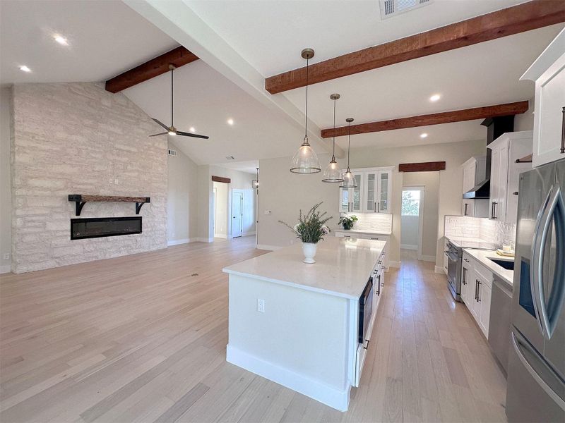 Kitchen with white shaker style cabinetry, open floor plan, with 15 ft vaulted ceiling in living room, 10 ft ceiling in kitchen, stainless steel appliances, level 4 quartz countertops, decorative light fixtures, and an expansive center island with dining bar.