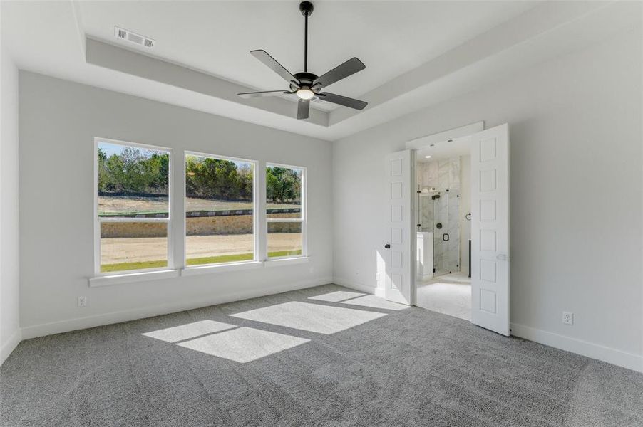 Unfurnished bedroom featuring carpet flooring, ceiling fan, and a tray ceiling