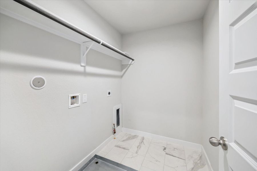 This photo shows a clean and compact laundry room with hookups for a washer and dryer, a tiled floor, and a hanging rod for clothes. This photo shows a clean and compact laundry room with hookups for a washer and dryer, a tiled floor, and a hanging rod for clothes.