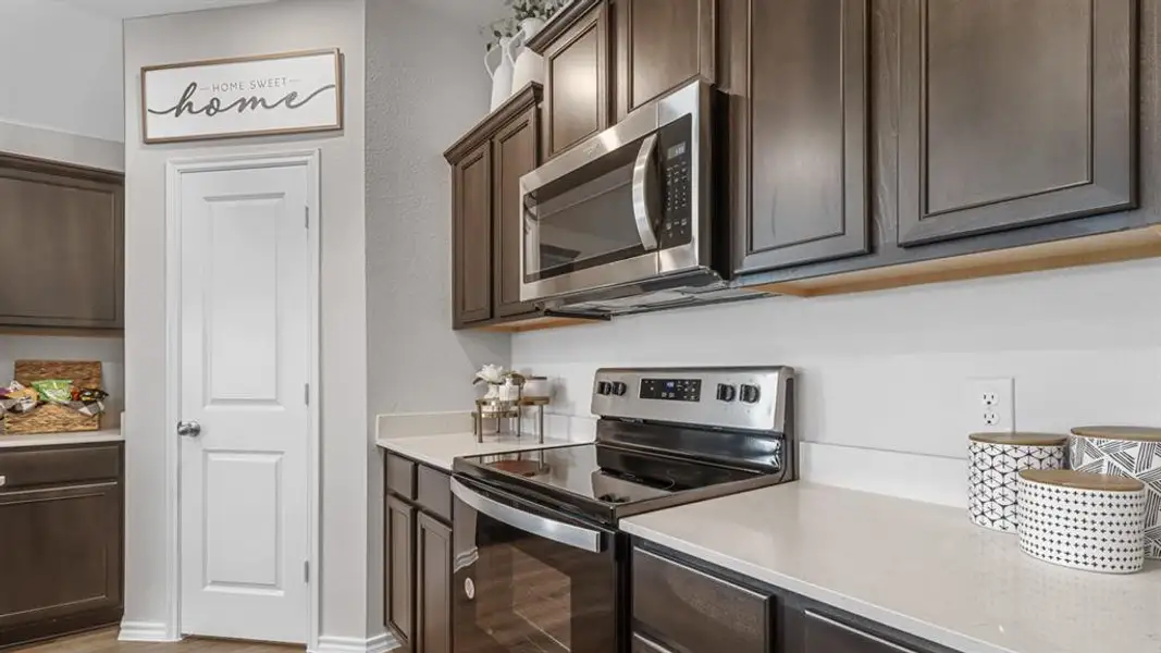 Kitchen with stainless steel appliances, dark wood finish cabinetry, and light stone countertops