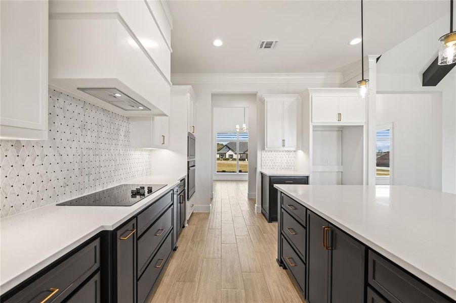 Dual tone kitchen with dual tone cabinets, light wood-style floors, black electric stovetop, light stone countertops, and decorative backsplash
