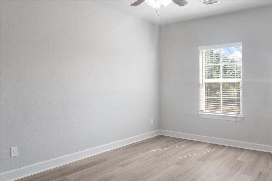This room features light-colored walls and flooring, a ceiling fan, and a bright window with blinds, offering a clean and airy space ideal for versatile use.